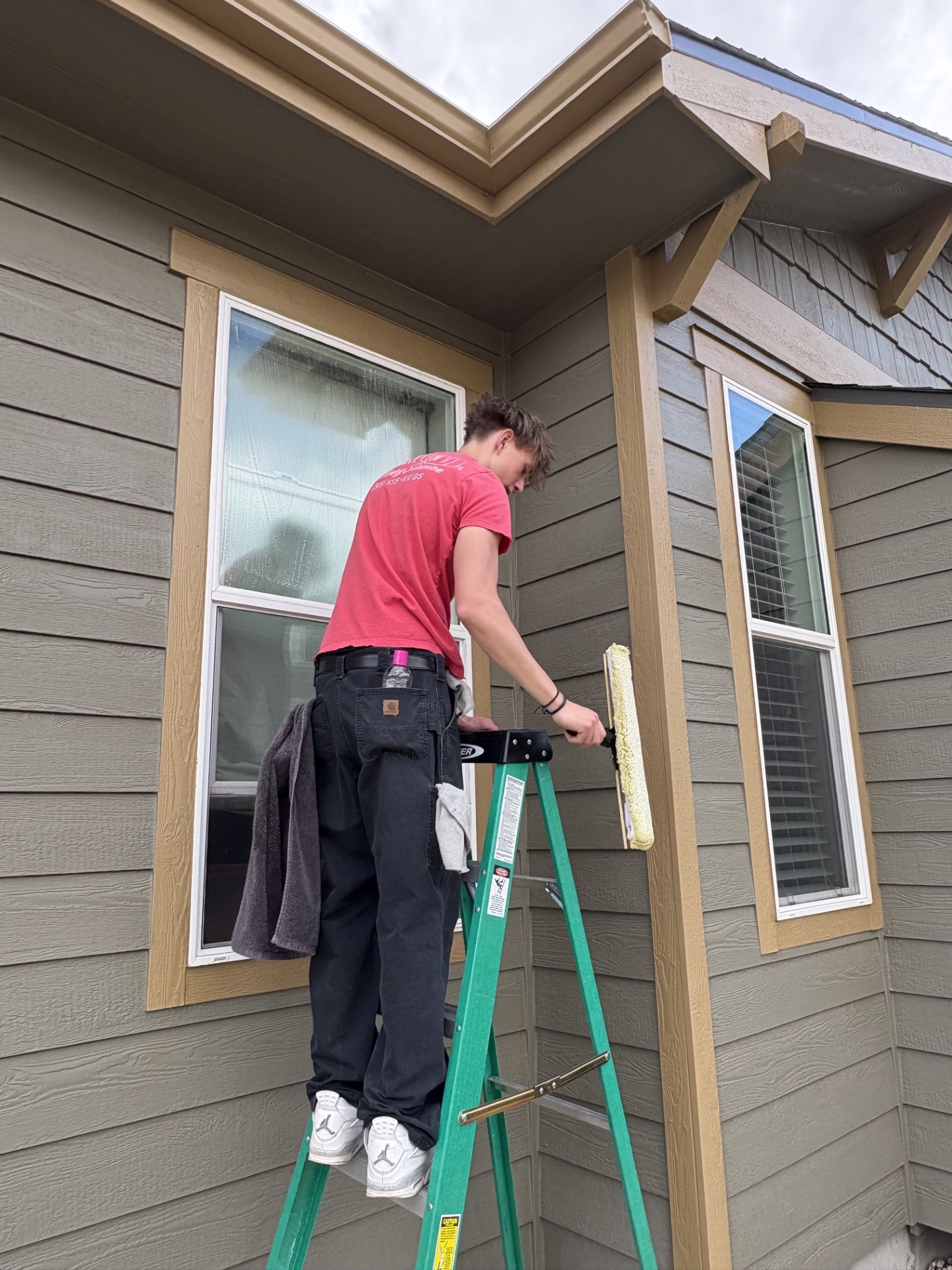 Red Wagon Windows team member cleaning an exterior window on a ladder